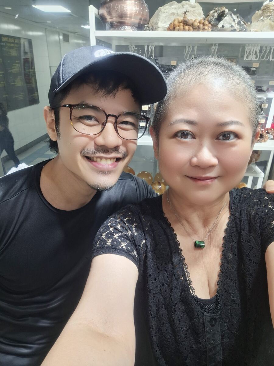 Jessica Woo taking a selfie with a smiling man in a cap and glasses in front of crystal shelves at Affinity Crystals, Singapore