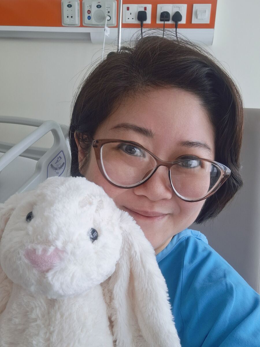Jessica Woo, founder of Affinity Crystals Singapore, smiling in a hospital room while holding a cream plush rabbit during breast cancer treatment