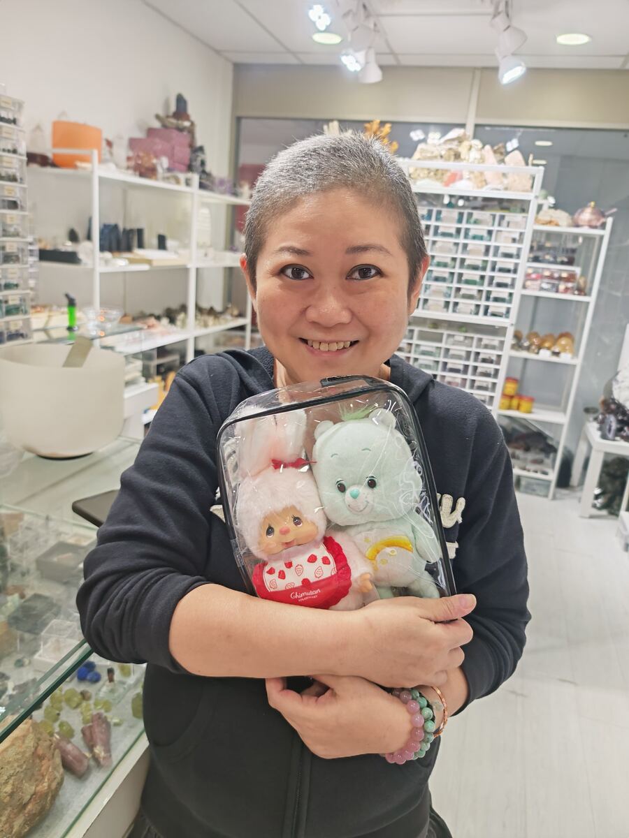Jessica Woo hugging two plush toys in a clear bag inside the Affinity Crystals shop in Chinatown, Singapore, with crystal shelves behind her